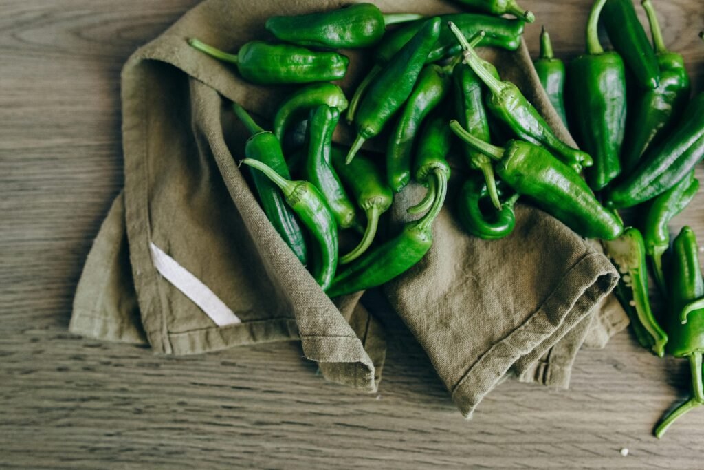 Top view of fresh green chilies on a rustic cloth and wooden table, vibrant and natural setting.