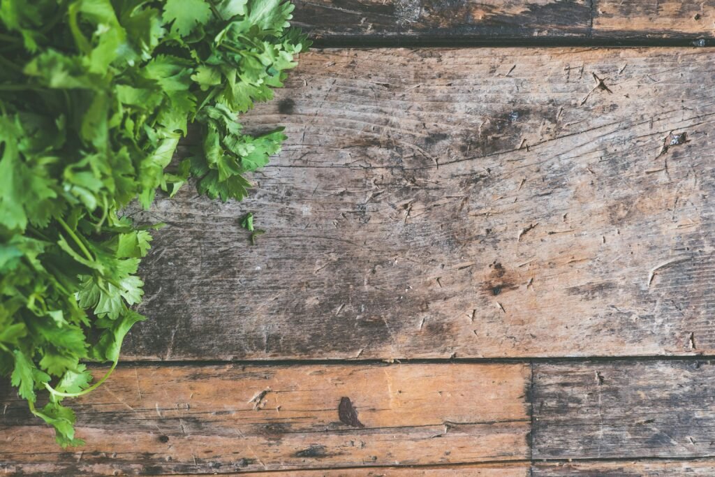 Top view of fresh cilantro leaves on a rustic wooden surface, showcasing natural texture and greenery.