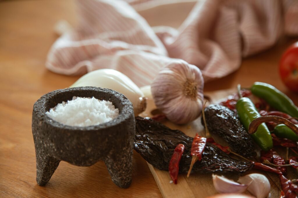 A collection of Mexican culinary ingredients including peppers, garlic, and salt on a kitchen table.